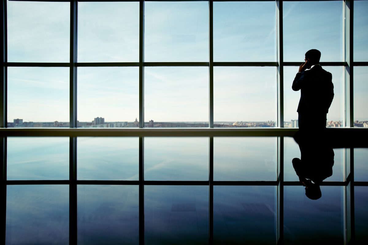 A silhouetted figure at a full-height window overlooking the water